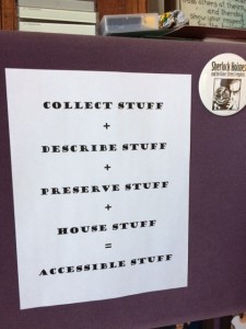 Image of the sign in Tim's office saying "Collect stuff + describe stuff + preserve stuff + house stuff = accessible stuff."