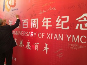 A picture of a person signing a large commemorative banner at the Xi’an YMCA anniversary celebration