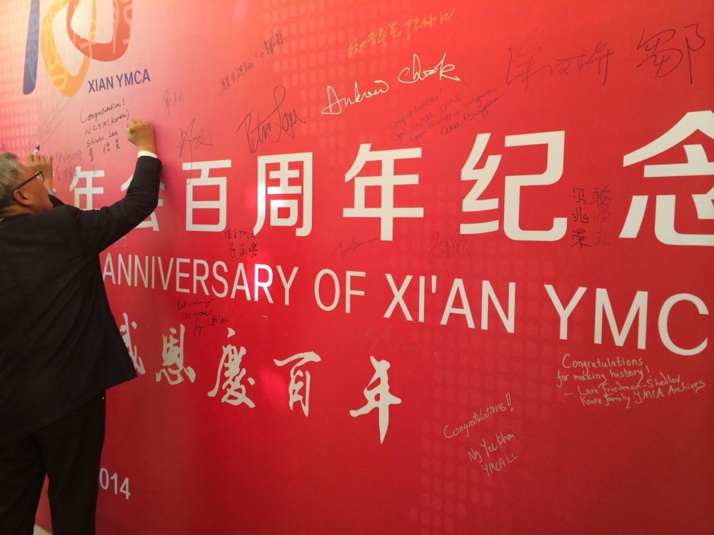 A picture of a hand signing a commemorative banner at the Xi’an YMCA anniversary celebration
