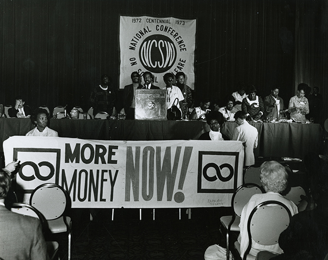 Photograph from the Social Welfare History Archives of the 1972-73 Centennial National Conference on Social Welfare. Participants hold a sign reading 'More Money Now!'