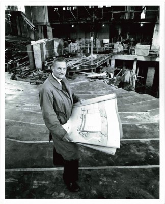 Tyrone Guthrie stands in what will be the auditorium of the Guthrie Theater. The iconic thrust stage is under construction behind him, 1962.