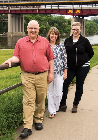 The River Life program’s Patrick Nunnally, left, and Joanne Richardson, right, with Kate McCready, Director of Publishing Services, stand on the banks of the great Mississippi River. Photo by Mark Engebretson