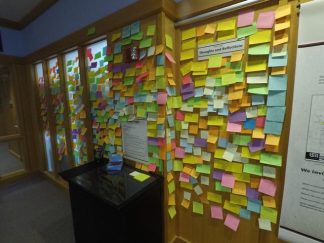 A wall covered in Post-It Notes with comments from exhibit viewers.