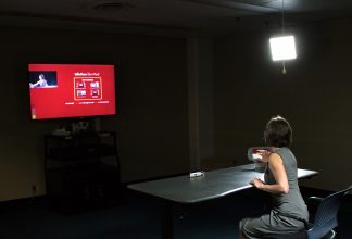 Photo of a woman using the 1:Button Studio. Also pictured are the table, the TV, the microphone, and one of the studio lights.