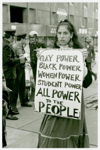 A young person holds a sign that reads "Gay Power, Black Power, Women Power, Student Power, All Power to the People"