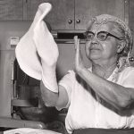 A woman tosses pizza dough with her hands. Image from the Immigration History Research Center Archives.