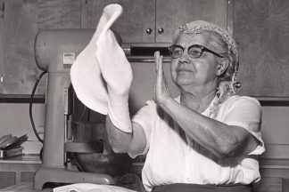 A woman tosses pizza dough with her hands. Image from the Immigration History Research Center Archives.