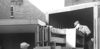 Black and white photo of movers using a fork lift to remove books from a truck.