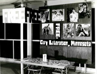 Historical photo of a table with pamphlets and a sign behind it that says FREE: Gay Liberation, Minnesota
