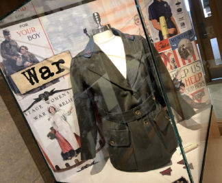 Exhibit vitrine with a YMCA women's uniform on a bust and war posters in the background