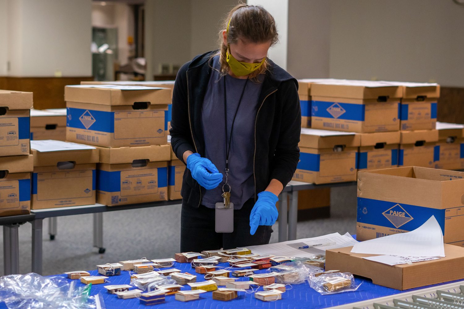 Conservation specialist Anna Shepherd is wearing a mask and gloves as she matches up pharmaceutical boxes with their corresponding bar codes.