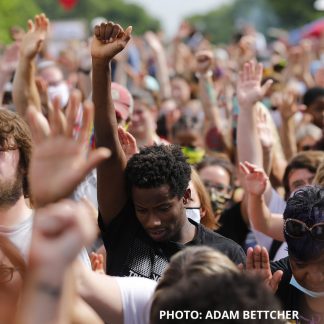 Photo by Adam Bettcher of a solemn crowd of people with hands and fists raised