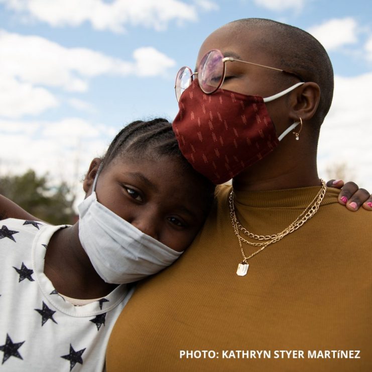 Photo by Kathryn Styer Martinez of two people embracing while wearing masks to protect against COVID