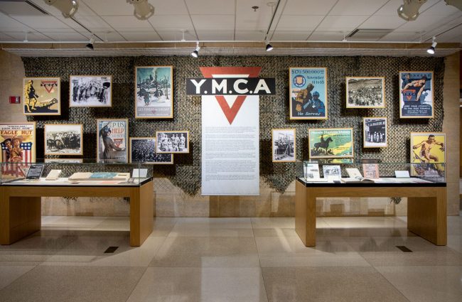 The main wall of the YMCA Exhibit, featuring framed photos. In front of the wall are two display cases.
