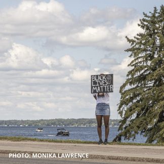 Photo by Monika Lawrence of person with Black Live Matter sign with a lake in the background