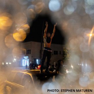 Photo by Stephen Maturen of person with hands raised standing on a vehicle
