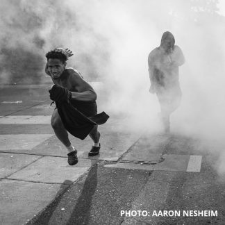 Photo by Aaron Nesheim of two people moving away from smoke or tear gas