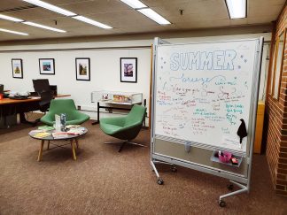 Magrath Library main floor with inviting furniture, whiteboard decorated for the summer, andwall of framed winning photos