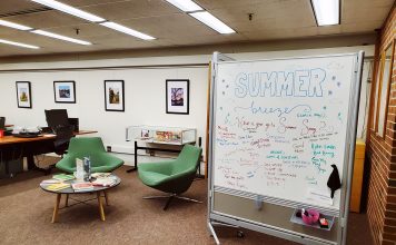 Magrath Library main floor with inviting furniture, whiteboard decorated for the summer, andwall of framed winning photos