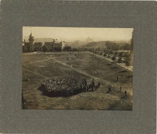 A historical U of M photo shows a group of people gathered on a field with Pillsbury Hall in the background