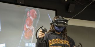 A person wearing a virtual reality headset stands in front of a screen showing an anatomical representation of an organ