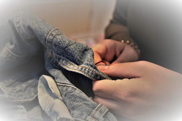 A close-up view of a pair of hands mending a denim garment.