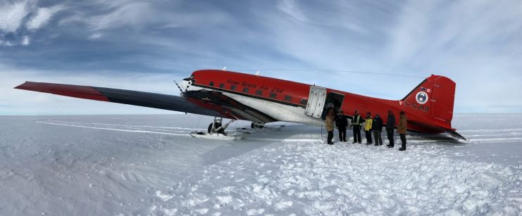 Photo of a small airplane on snow with group of people standing near