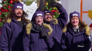 several people in purple snow suits and knit caps, in a snowy setting.