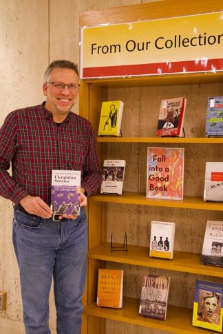 Brian Vetruba holding "Ukranian Stories" near a bookshelf.