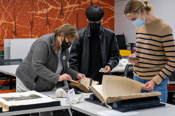 Three people are looking at images found in rare books set up on a table.