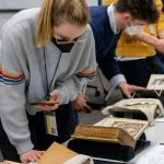 Several students standing and examining rare books placed on long tables.