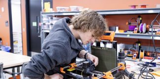 Student operating a 3D printer atop a desk.
