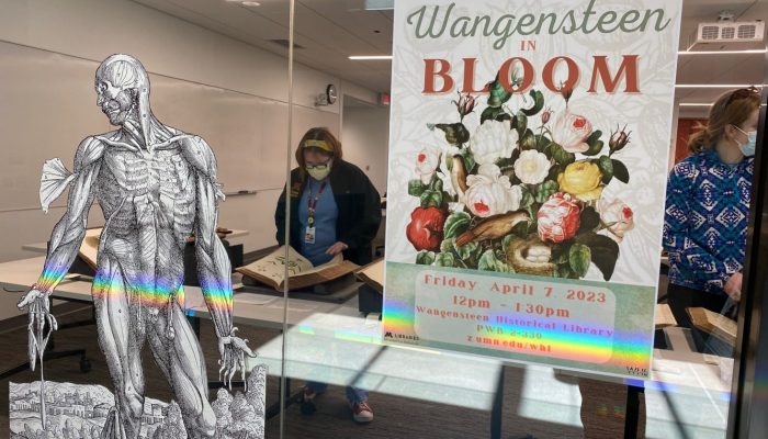 Exhibit poster displayed on the glass outside of the Wangensteen Classroom, where the pop up exhibit "Wangensteen in bloom" took place. An attendee can be seen in the background looking at a book on display.