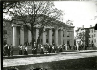 Black and white image from the University Archives of Burton Hall, a columned building. Students appear in the foreground milling about.